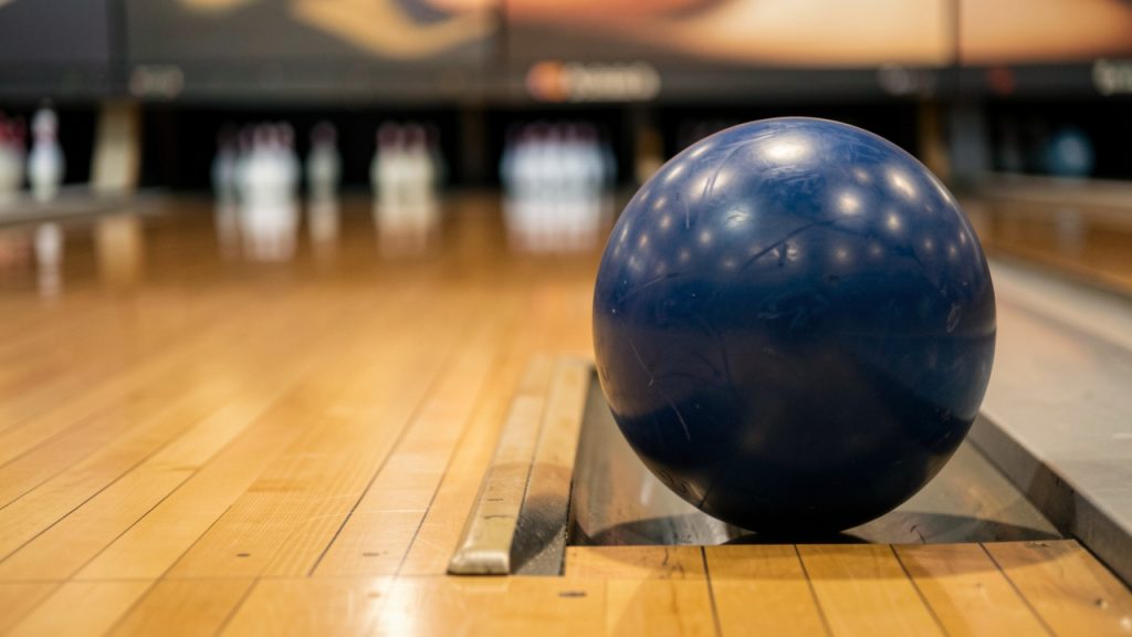 Une boule de bowling bleue immobilisée dans la rigole à côté d’une piste brillante, avec des quilles floues au loin.